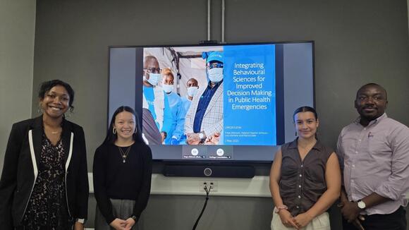 The group of 4 LSTM students stand in front of a TV screen presenting their work